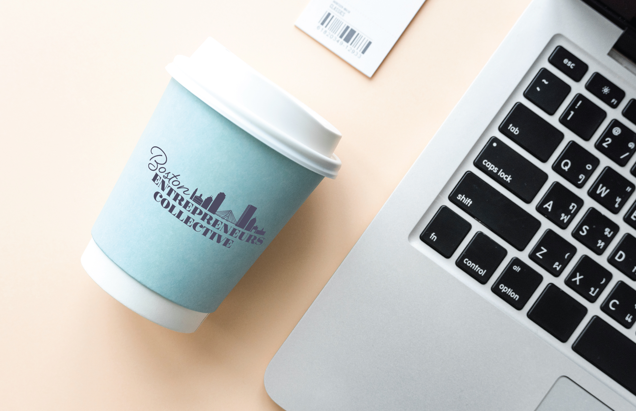 A disposable coffee cup with logo laying next to open laptop in a staged branding photo.