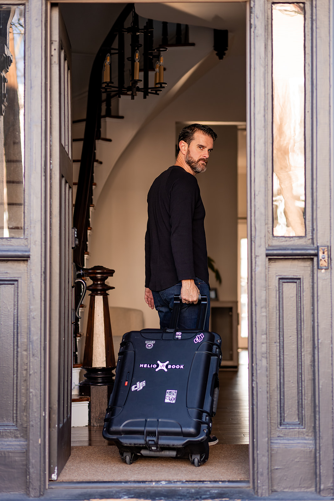 real estate photographer entering home, rolling his gear bag behind him while looking over his shoulder and out the front door. 