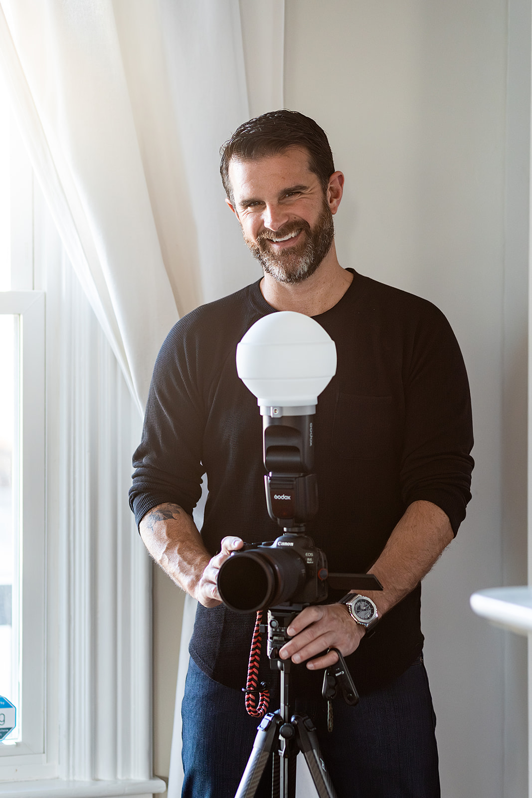 Photographer posing near window with camera on tripod