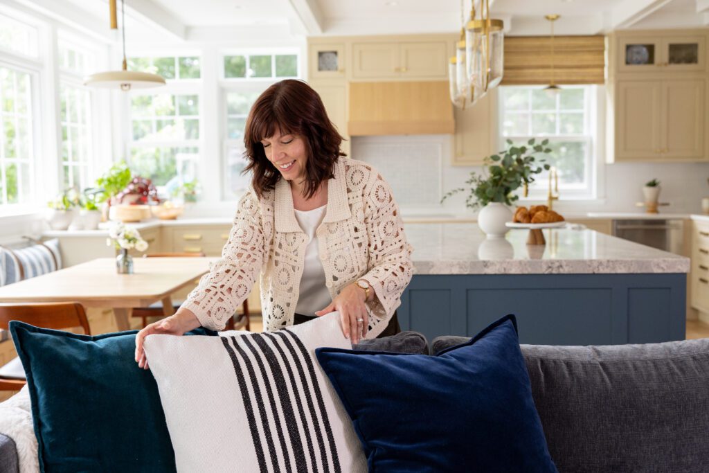 photo of woman standing behind a couch, adjusting the pillows. 